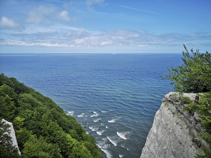 Blick auf das Meer von einer Steilküste mit grünen Bäumen im Vordergrund.