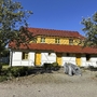 Ferienhaus mit gelber Tür im Feriendorf, umgeben von Bäumen bei sonnigem Wetter.