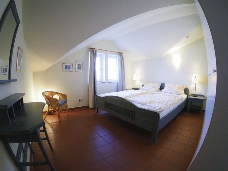 Helles Schlafzimmer mit Doppelbett und Schreibtisch, schlichte Dekoration.