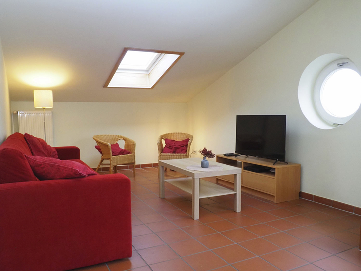Wohnzimmer mit rotem Sofa, TV, Couchtisch und Dachfenster.