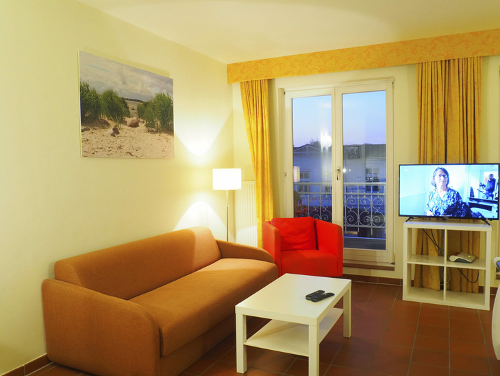 Wohnzimmer mit Sofa, Sessel, TV und Balkonblick in einer Ferienwohnung.