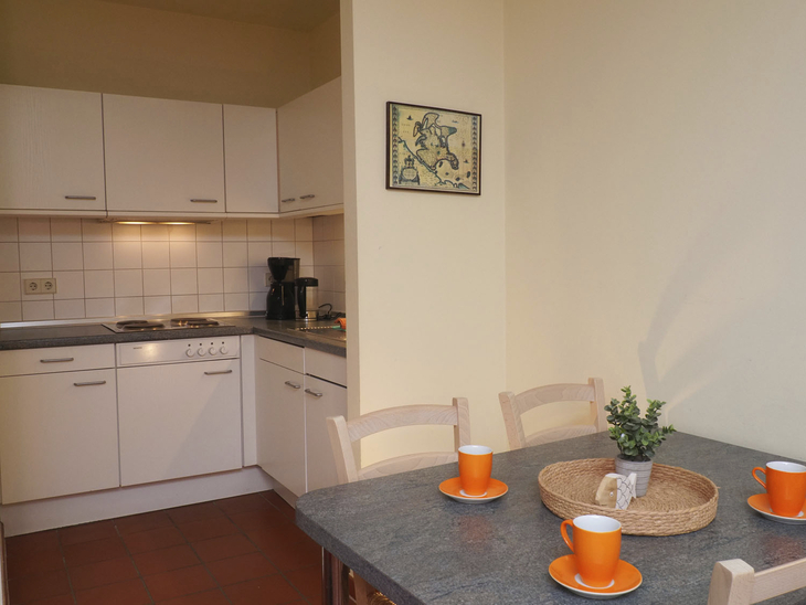 Essbereich mit Tisch, vier orange Tassen, kleiner Kücheneinblick im Hintergrund.
