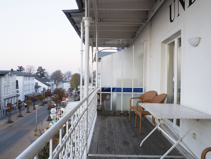 Balkon einer Wohnung mit Tisch und Stühlen, Ausblick auf eine Straße und umliegende Gebäude.