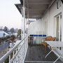 Balkon einer Wohnung mit Tisch und Stühlen, Ausblick auf eine Straße und umliegende Gebäude.