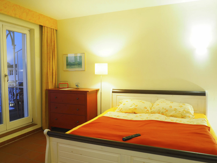 Helles Schlafzimmer mit Doppelbett, Nachttisch und Lampe in einer Ferienwohnung.