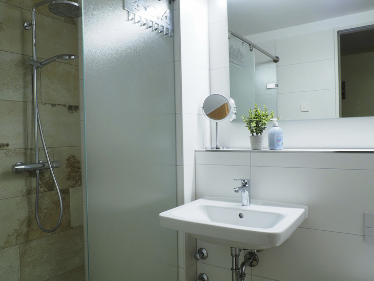 Bad mit Dusche, Waschbecken und Spiegel, modern und hell gestaltet.