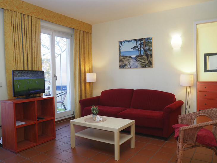 Wohnzimmer mit rotem Sofa, Couchtisch, Fernseher und Balkonzugang.