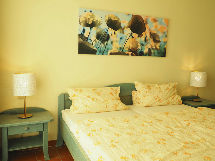 Doppelbett mit Blumenbezug in heller Wohnung mit zwei Nachttischen und Lampen.