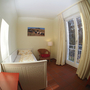 Helles Zimmer mit Bett, Sessel, Lampe und großem Fenster mit Vorhängen.