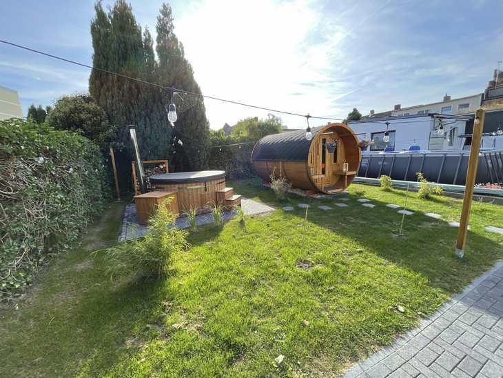 Garten mit Sauna und Whirlpool, umgeben von Rasen und Bäumen.