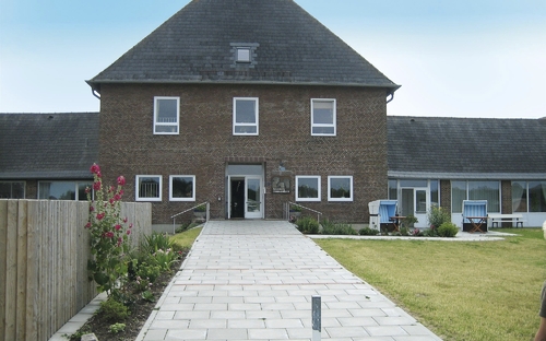 Gebäude mit rotem Ziegeldach und gepflastertem Weg, umgeben von Garten auf Sylt.