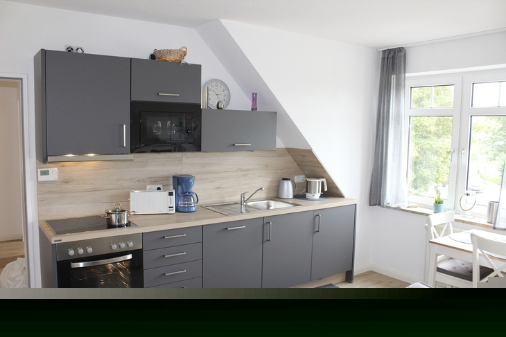 Moderne Einbauküche mit grauen Schränken und Esstisch in heller Ferienwohnung.