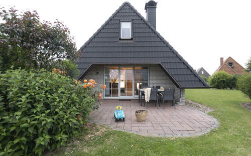 Haus mit schwarzem Dach, Terrasse, Stuhl und Spielzeugauto im Garten.