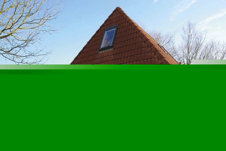 Ferienhaus mit rotem Dach und Giebelfront, umgeben von Rasen und Büschen.