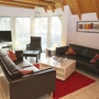 Wohnzimmer mit zwei Sofas, Sessel, Couchtisch, Fernseher und großen Fenstern.