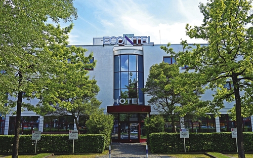 Eingangsbereich des Econtel Hotels in München mit Bäumen und blauen Himmel.