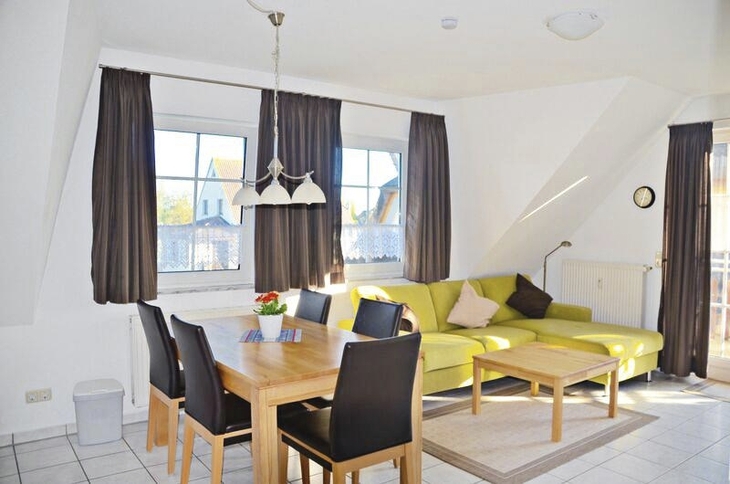 Wohnzimmer mit Esstisch, Ecksofa und großen Fenstern.