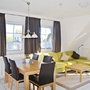 Wohnzimmer mit Esstisch, Ecksofa und großen Fenstern.