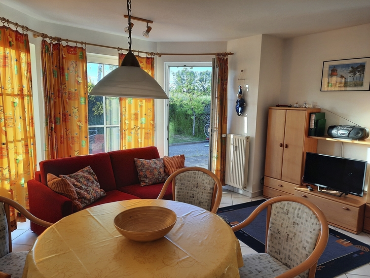 Wohnzimmer mit roten Sofa, Esstisch, TV und Fenstern mit gelben Vorhängen.