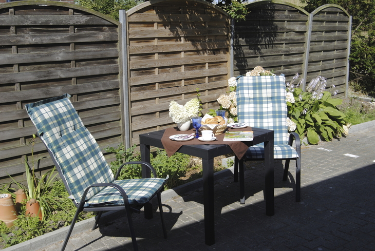 Gartentisch und zwei Stühle vor Holzzaun, gedeckt mit Blumen und Geschirr.