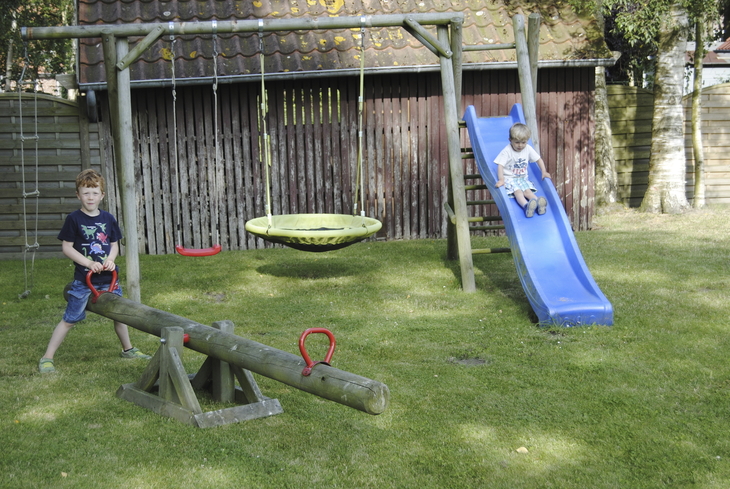 Zwei Kinder spielen auf einem Spielplatz mit Rutsche und Wippe.
