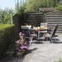 Gartenterrasse mit Tisch, Stühlen und blühenden Blumen im Sonnenschein.