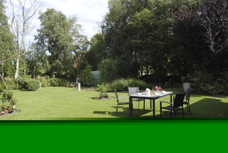 Ein Garten mit Rasenfläche und einem Tisch mit Stühlen im Vordergrund.