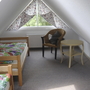 Dachzimmer mit zwei Betten, Stuhl und Tisch, Fenster mit Vorhängen.