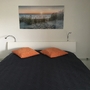 Bett mit dunkler Tagesdecke und zwei orangefarbenen Kissen in einem Schlafzimmer.