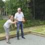 Personen spielen Boccia auf einem Kiesplatz neben einem Zaun.