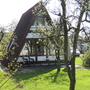 A-förmiges Ferienhaus in sonnigem, grünem Garten mit Bäumen.