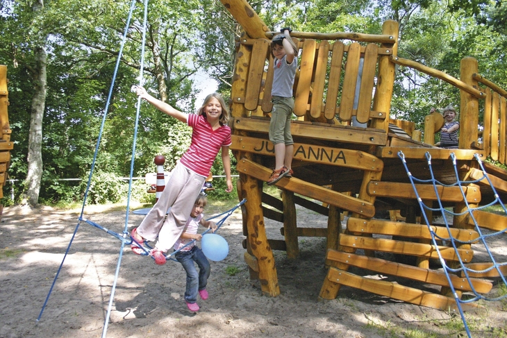 Kinder spielen auf einem hölzernen Abenteuerspielplatz im Freien.