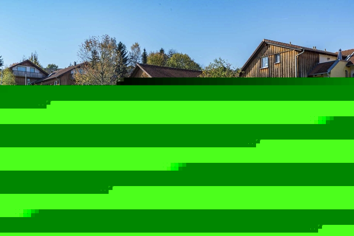 Mehrere Menschen sitzen im Freien vor Holzgebäuden an einem sonnigen Tag.