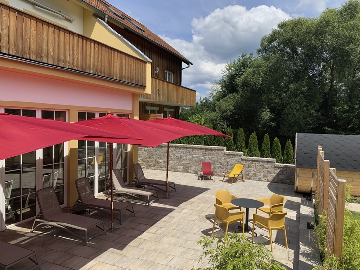 Terrasse mit Liegestühlen, roten Schirmen und umliegenden Bäumen im Sauna-Außenbereich.
