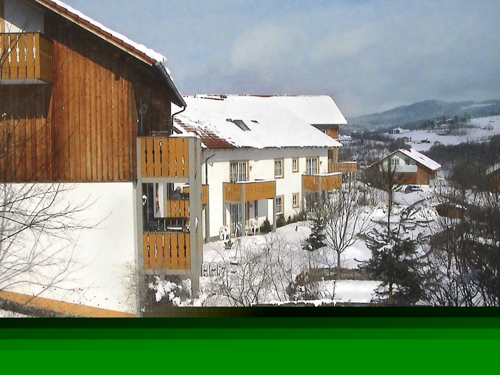 Feriendorf im Winter mit schneebedeckten Holzhäusern und Hügeln im Hintergrund.