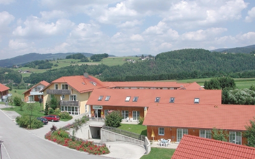 Panorama eines Feriendorfs mit roten Dächern und grüner Hügellandschaft im Hintergrund.