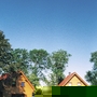 Zwei gelbe Ferienhäuser vor grünem Wald und blauem Himmel.