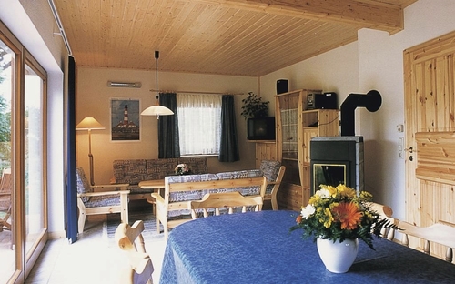 Gemütliches Wohnzimmer mit Holzmöbeln, Esstisch und Kaminofen.