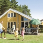 Familie vor einem gelben Ferienhaus im Grünen an einem sonnigen Tag.