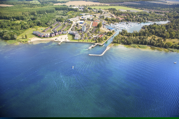 Luftbild eines Ferienparks an einem See mit umliegendem Wald und Bootsanlegestellen.