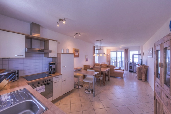 Moderne Ferienwohnung mit offener Küche und Wohnbereich, Blick auf Fenster und Balkon.
