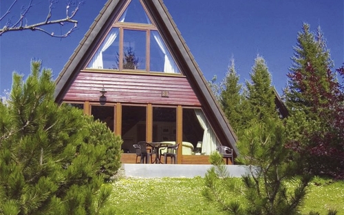 A-förmiges Holzhaus mit Glasfront vor blauem Himmel.