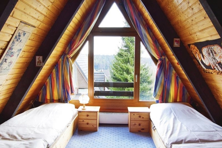 Zimmer mit zwei Betten in einem Dachgeschoss mit Holzverkleidung und bunten Vorhängen.