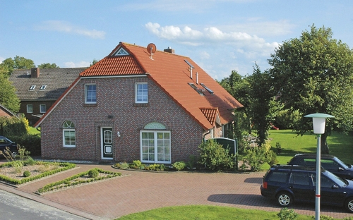 Ziegelhaus mit rotem Dach und Garten, davor gepflasterte Auffahrt mit Autos.