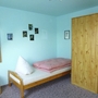Ein einfaches Schlafzimmer mit Einzelbett, Holzkleiderschrank und blauen Wänden.