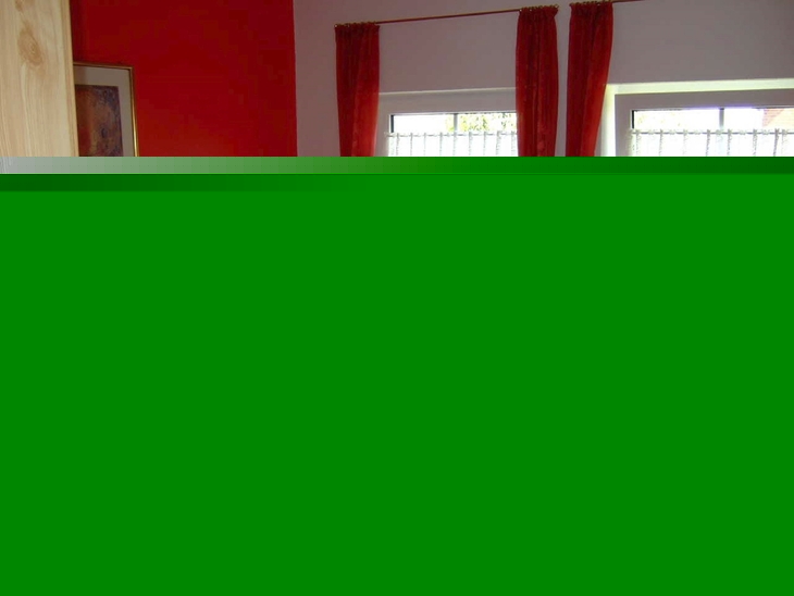 Schlafzimmer mit Holz-Doppelbett, roten Vorhängen und orangefarbener Bettwäsche.