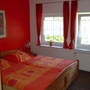 Schlafzimmer mit Holz-Doppelbett, roten Vorhängen und orangefarbener Bettwäsche.