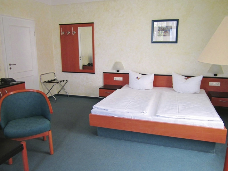 Hotelzimmer mit Doppelbett, zwei Nachttischen, Stuhl und Spiegel.