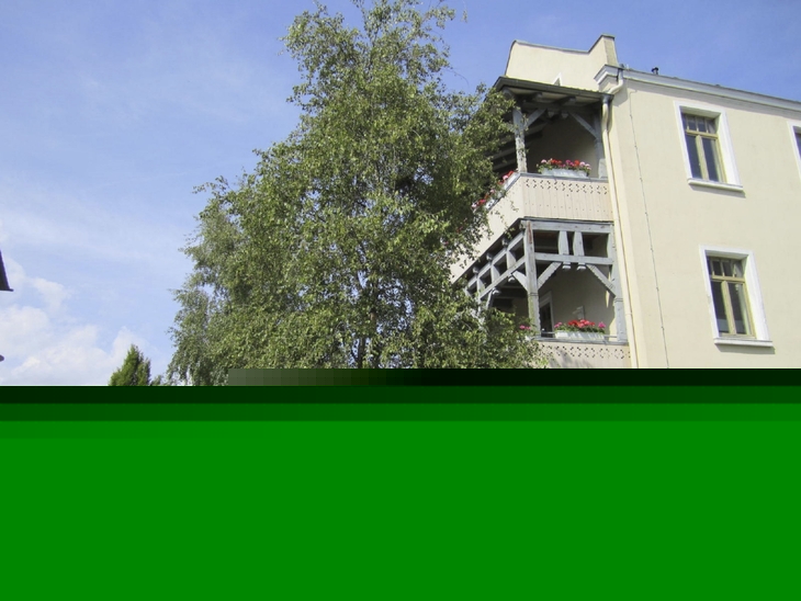 Mehrstöckiges Gebäude mit Balkonen, Baum im Vordergrund, sonniges Wetter.