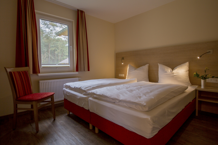 Hotelzimmer mit Doppelbett, Fenster mit Vorhang, Stuhl und Holzboden.